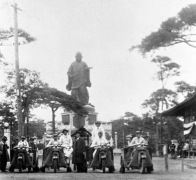 Caravan of three-wheeled trucks in front of statue of the Venerable Nichiren, Fukuoka prefecture
